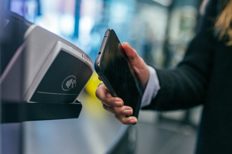 A person holding a credit card and a phone at a checkout counter receiving a paper receipt.