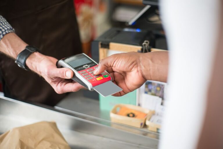 A cashier processes a customer's payment using a card reader at a small retail counter.