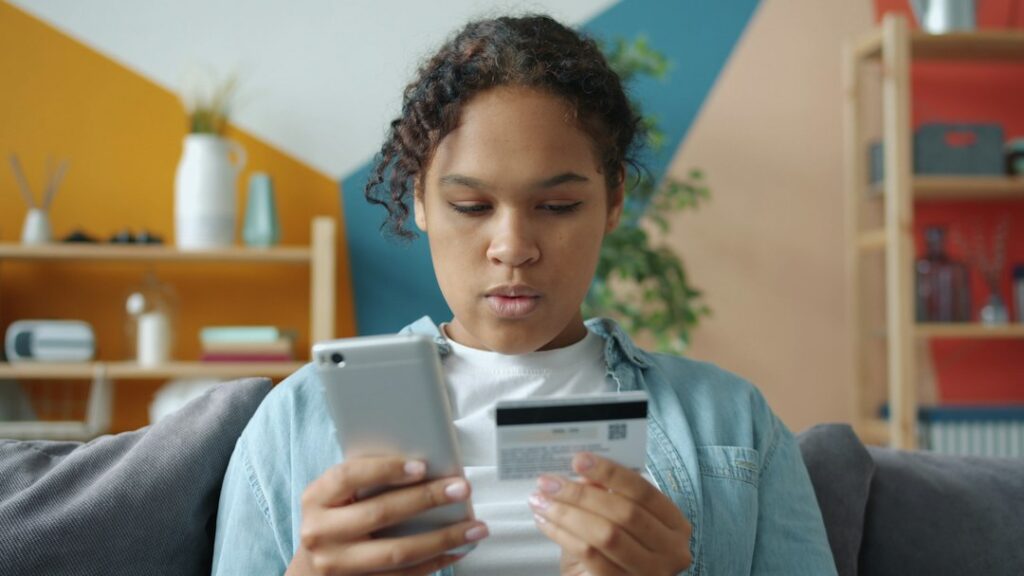 Person reviewing bank transactions and payment alerts on a laptop beside a locked smartphone.